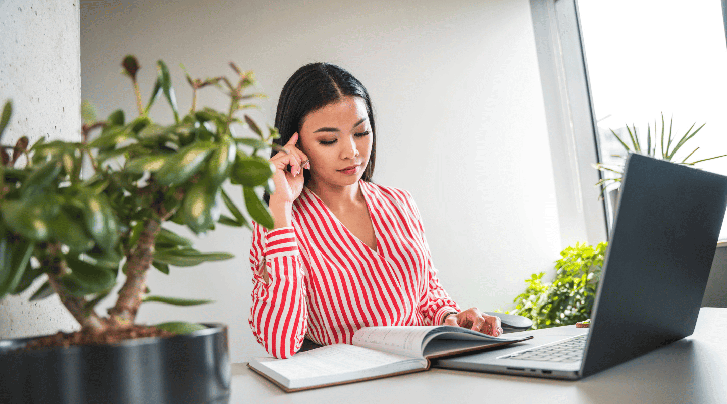 Professional woman focused on reading a book next to a laptop, representing virtual assistant services.